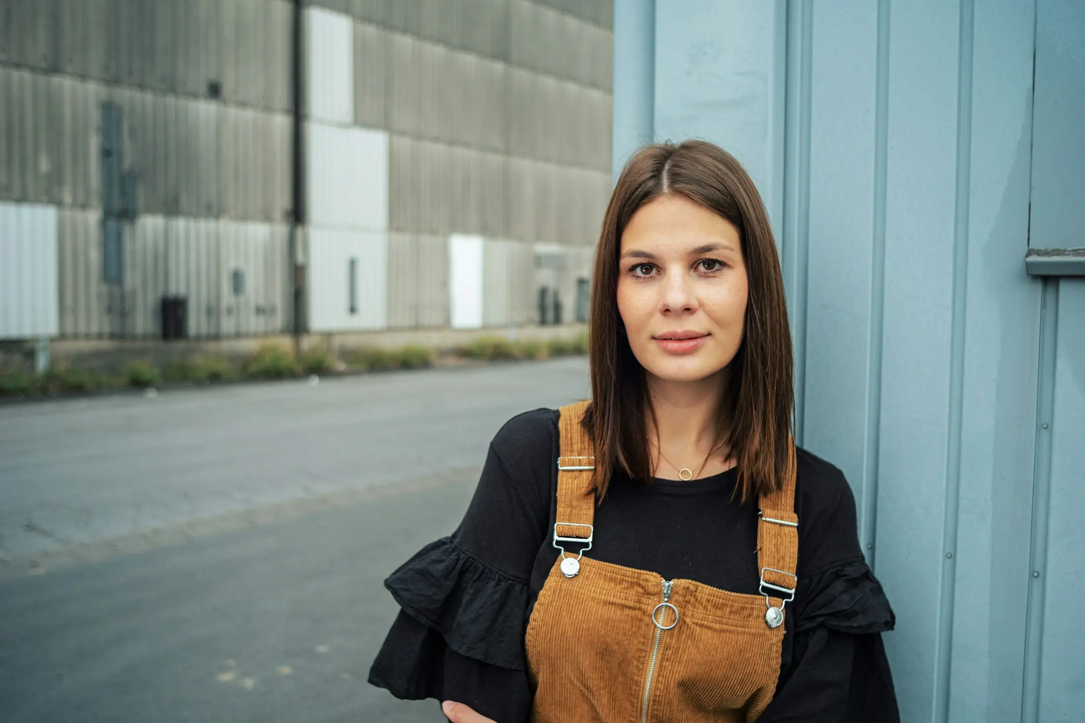 Woman with shoulder-length brown hair standing at ease against a blue wall outdoors