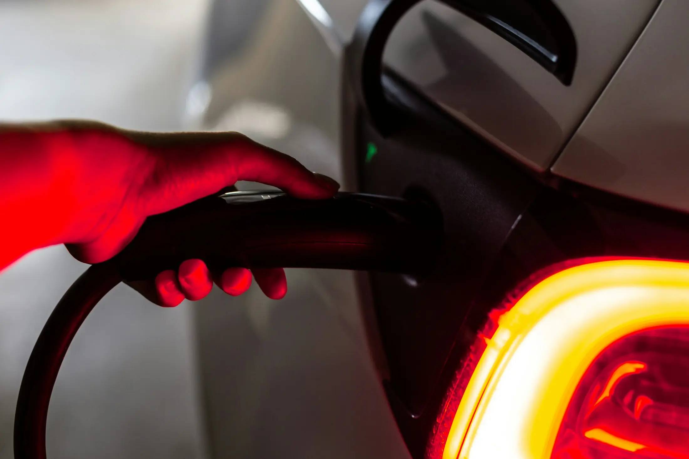 Charging cable plugged into an electric car beside a glowing tail light