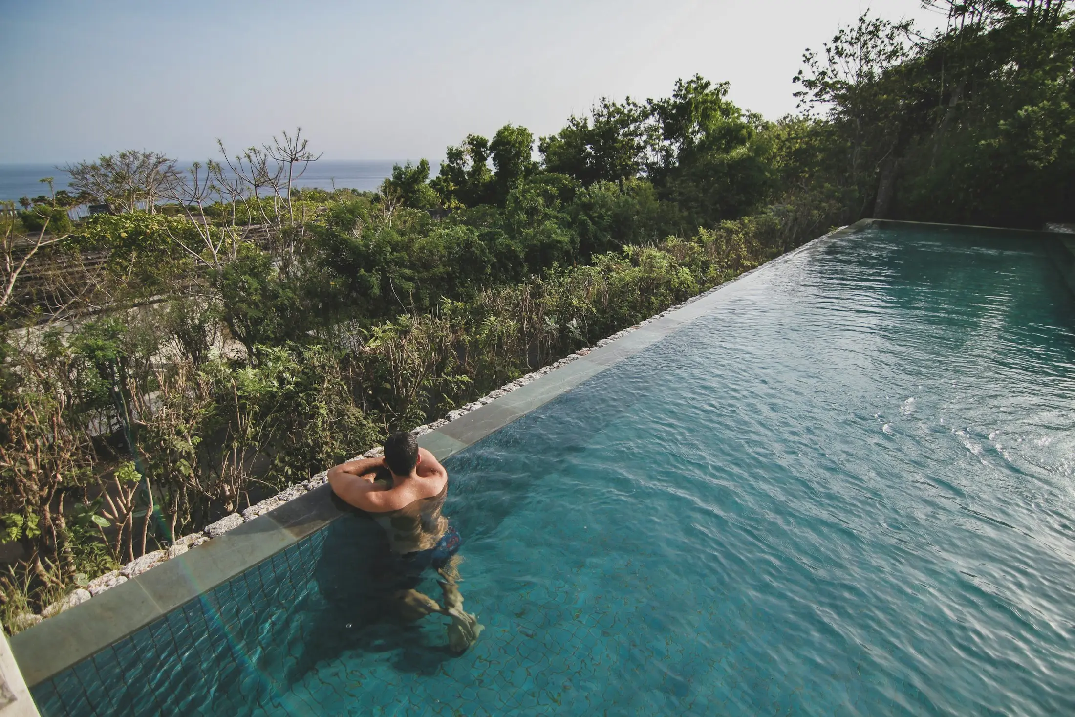 Woman relaxing in an infinity pool overlooking tropical jungle