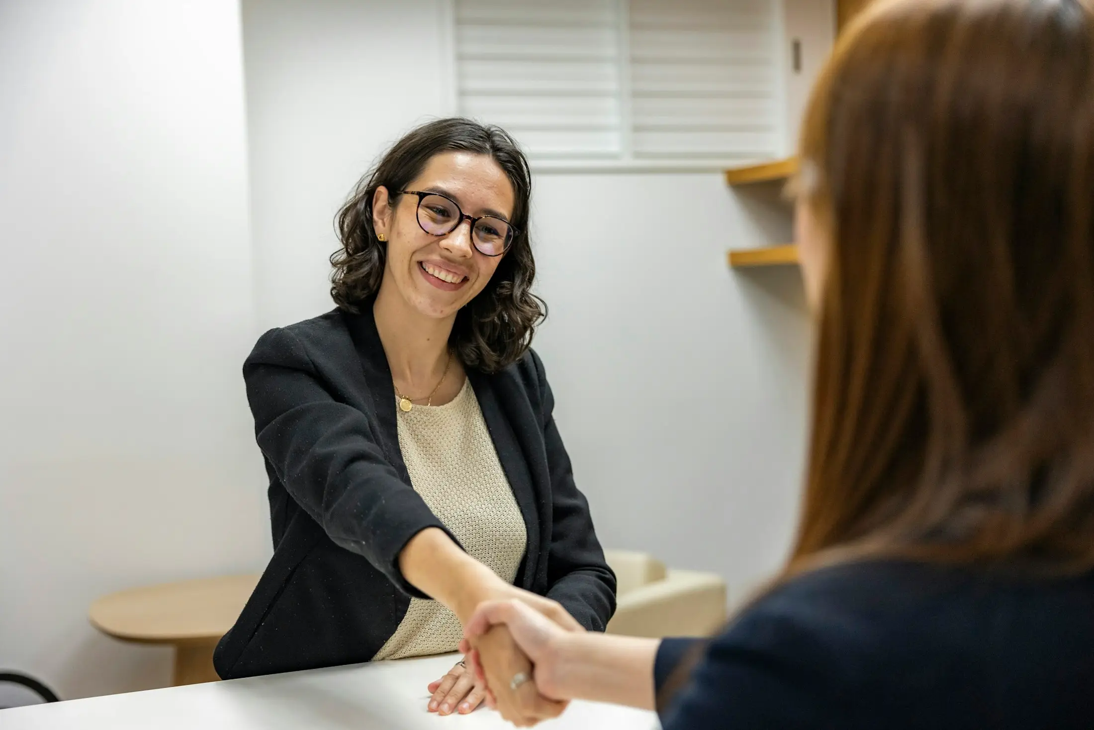 Two women shaking hands across a desk after agreeing on the next steps