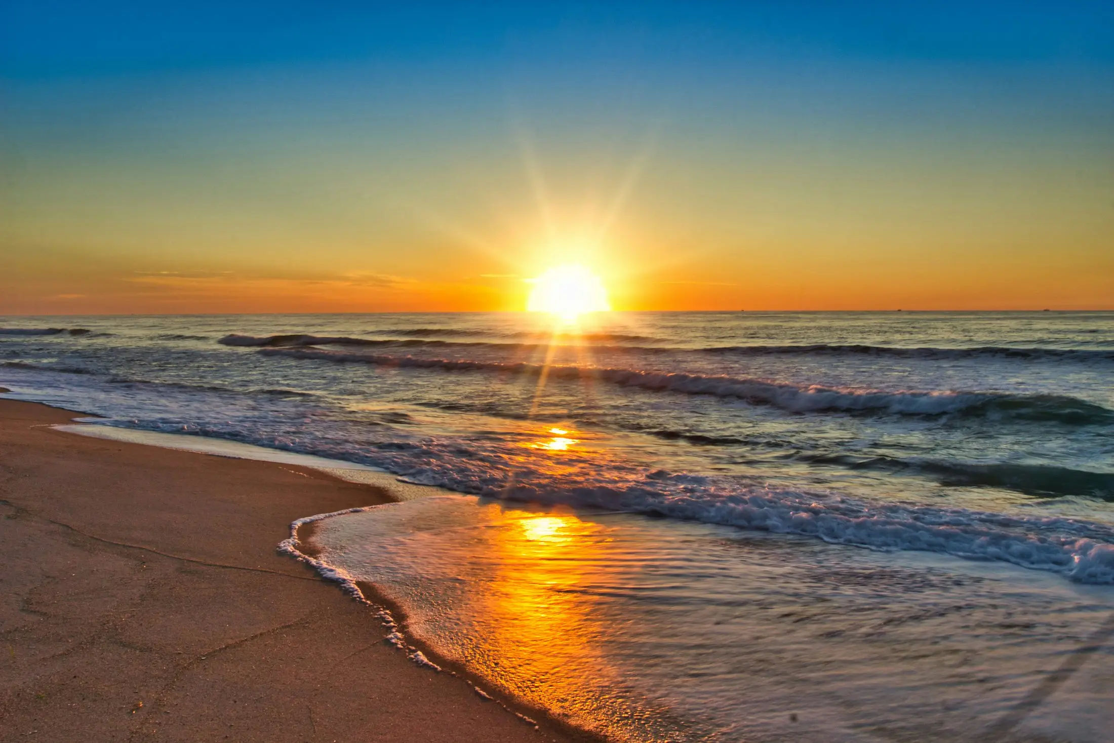 Sun rising over gentle waves rolling onto a golden beach