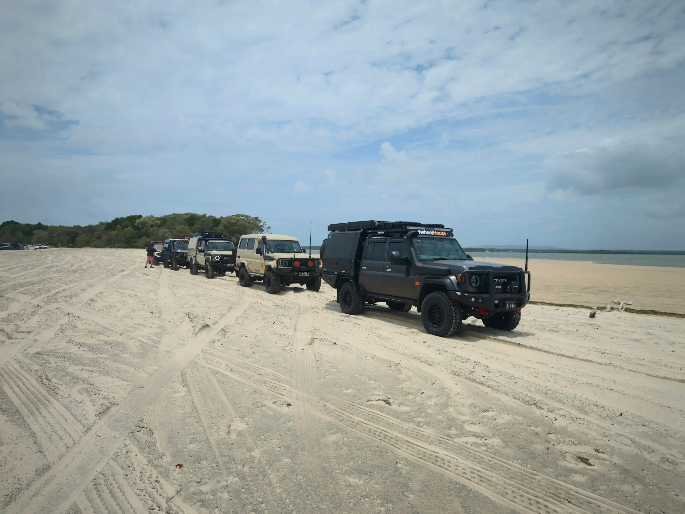 A convoy of kitted-out 4WDs driving along a wide sandy beach on K’gari