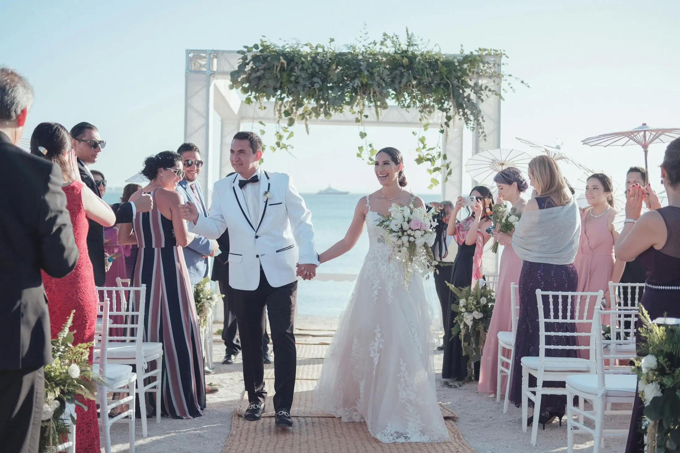 Newlyweds walking down a beach wedding aisle as guests cheer